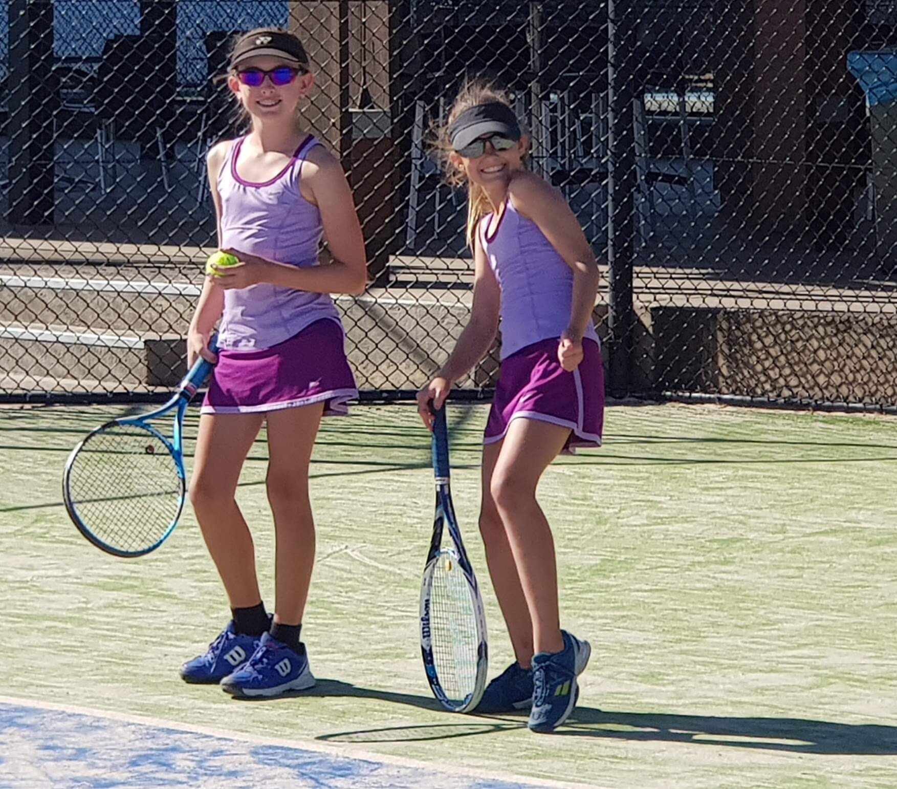Girls in mataching tennis uniforms playing tennis on court