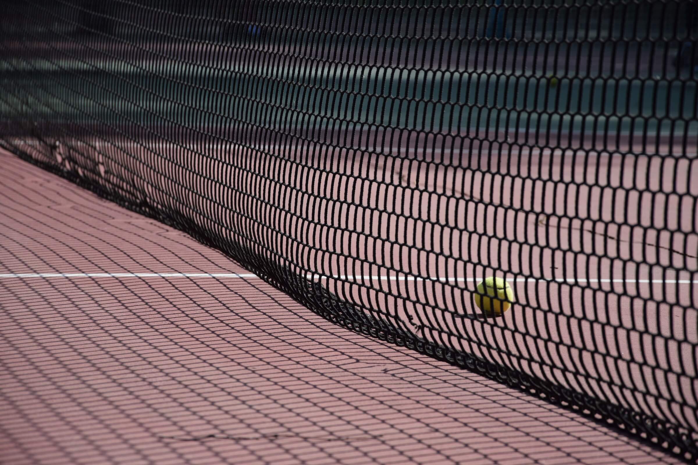 Tennis netting casting shadows over red tennis court