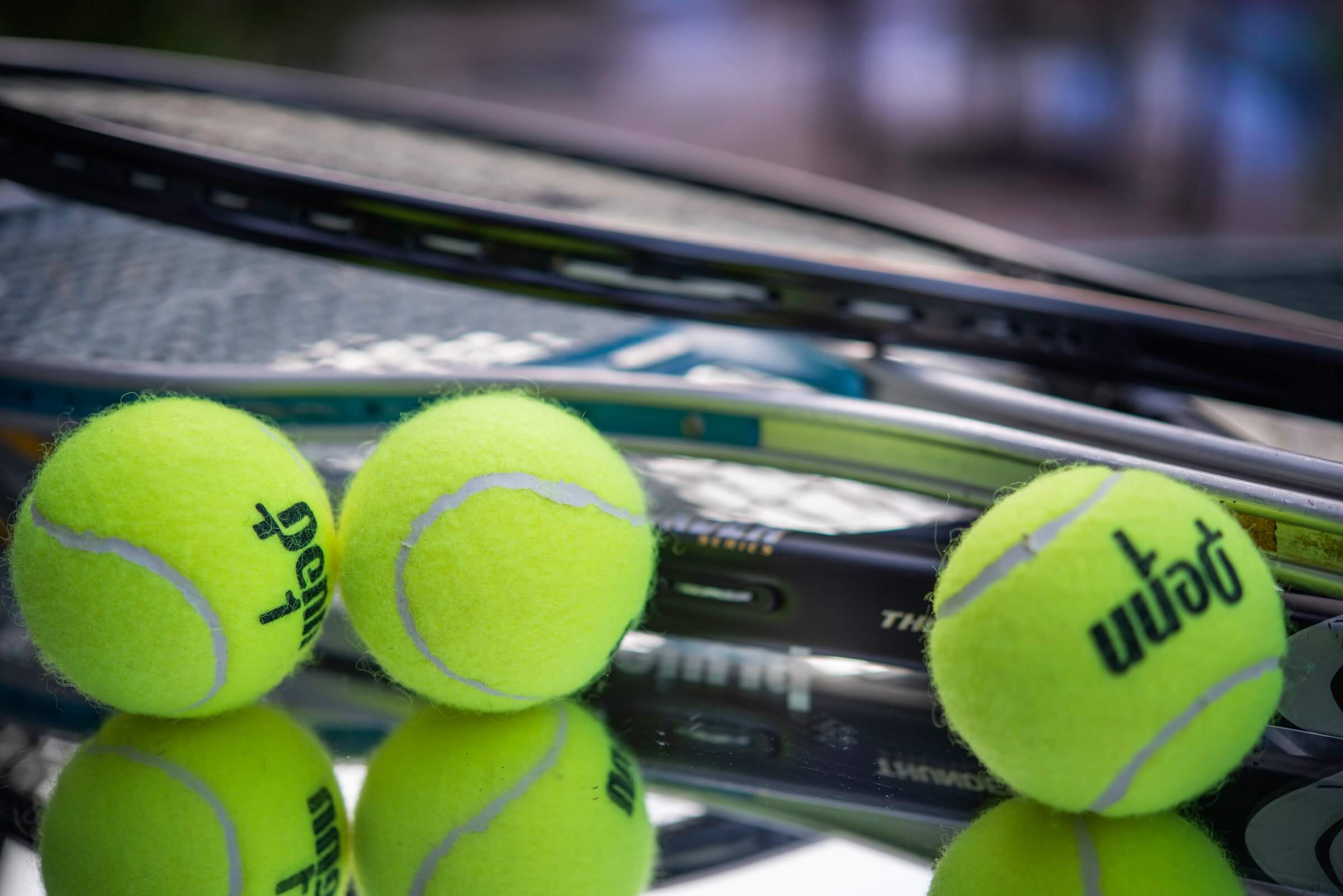 Close up of tennis balls and tennis racquets with wet court backdrop