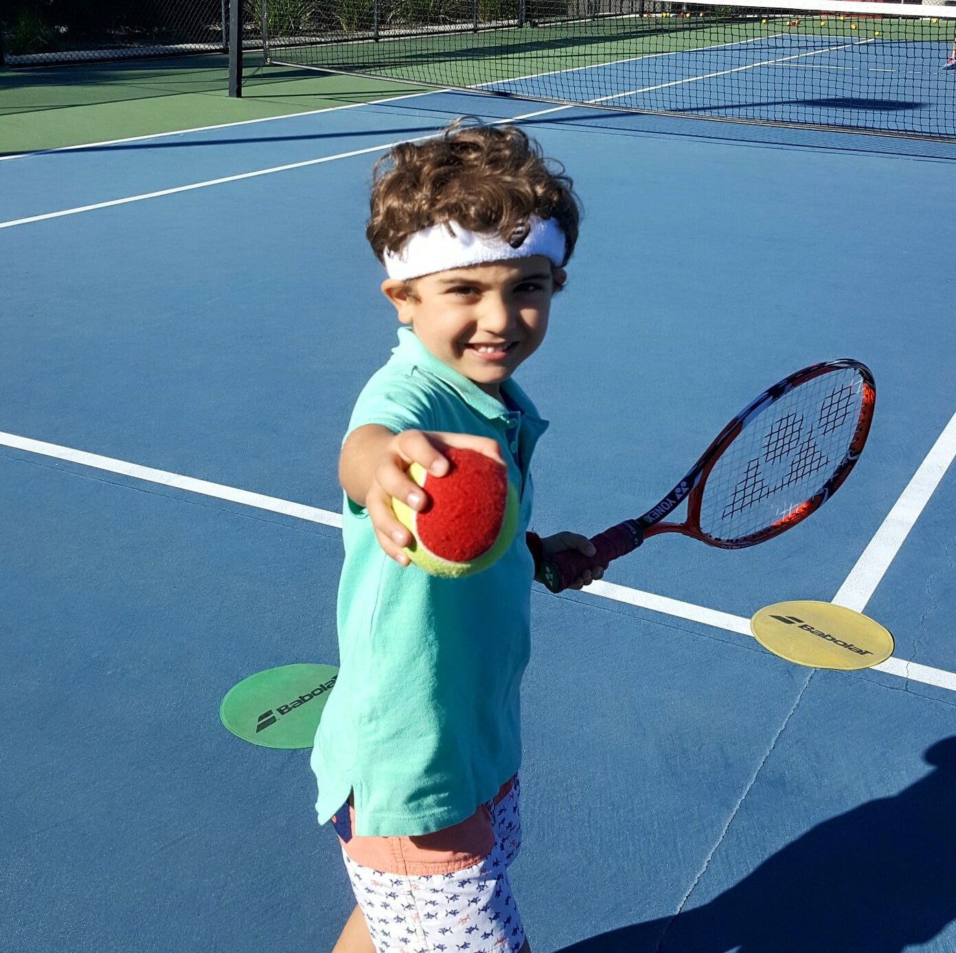 Kid playing tennis handing ball to camera at Redcliffe Tennis Centre